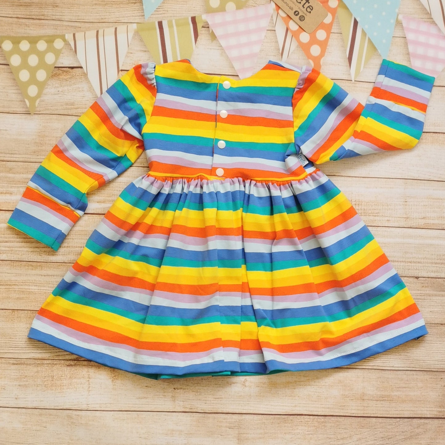 Rear view of the colourful red rainbow striped back popper dress. Showing the 9-12 months and over version with poppers down to the waist.