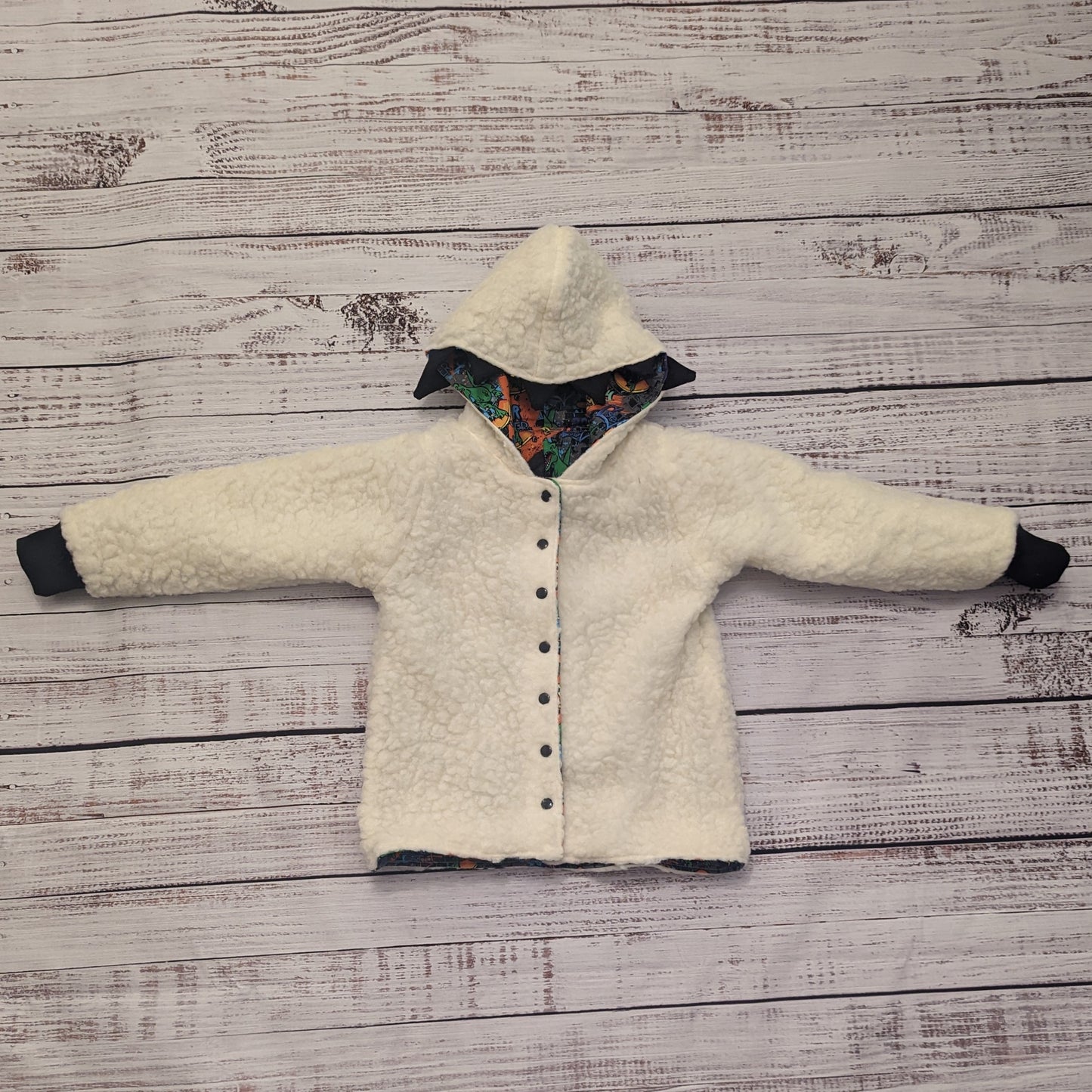 The ferociously cool street Dino reversible coat, shown with dinosaur teeth and spines for added fun. Handmade using street dino cotton French terry, black cotton ribbing and sherpa fur. Showing the reverse as a sherpa fur hoodie.
