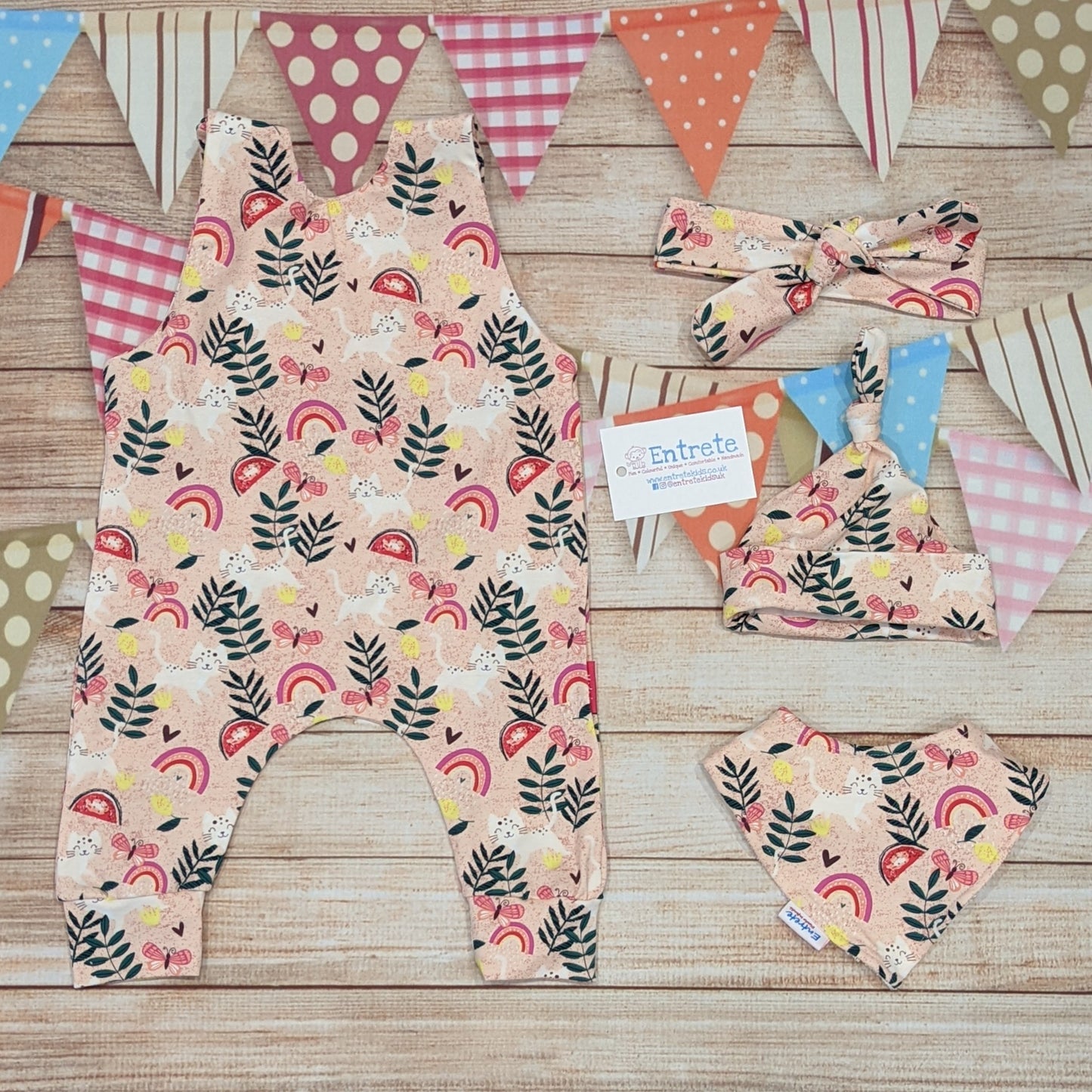 Playful pink cats sleeveless romper, handmade using pink cats cotton jersey. Shown from the rear with matching headband, tie top hat and bamboo bib.