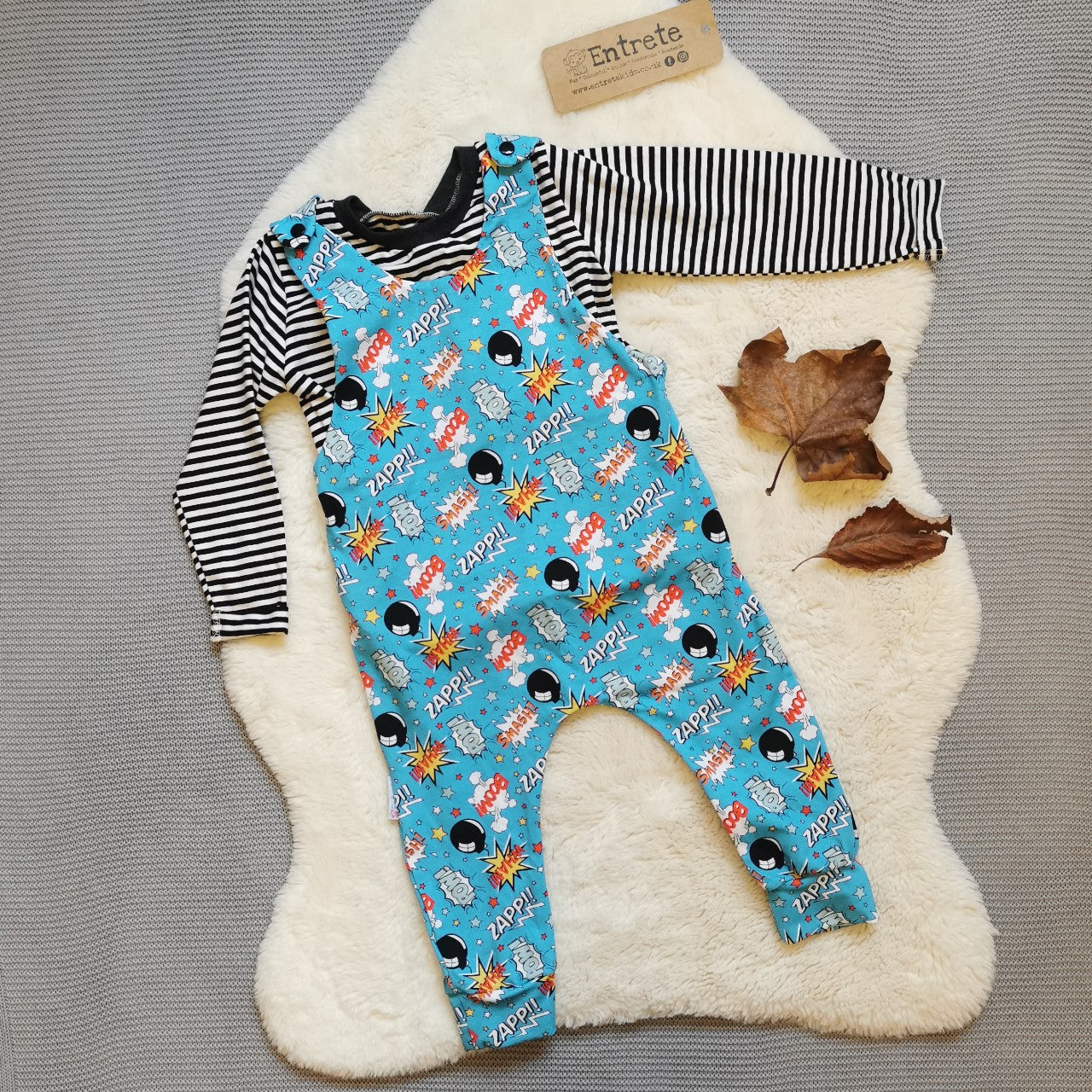 The vibrant and fun turquoise boom pow wow sleeveless romper, shown with a monochrome striped top (sold separately).