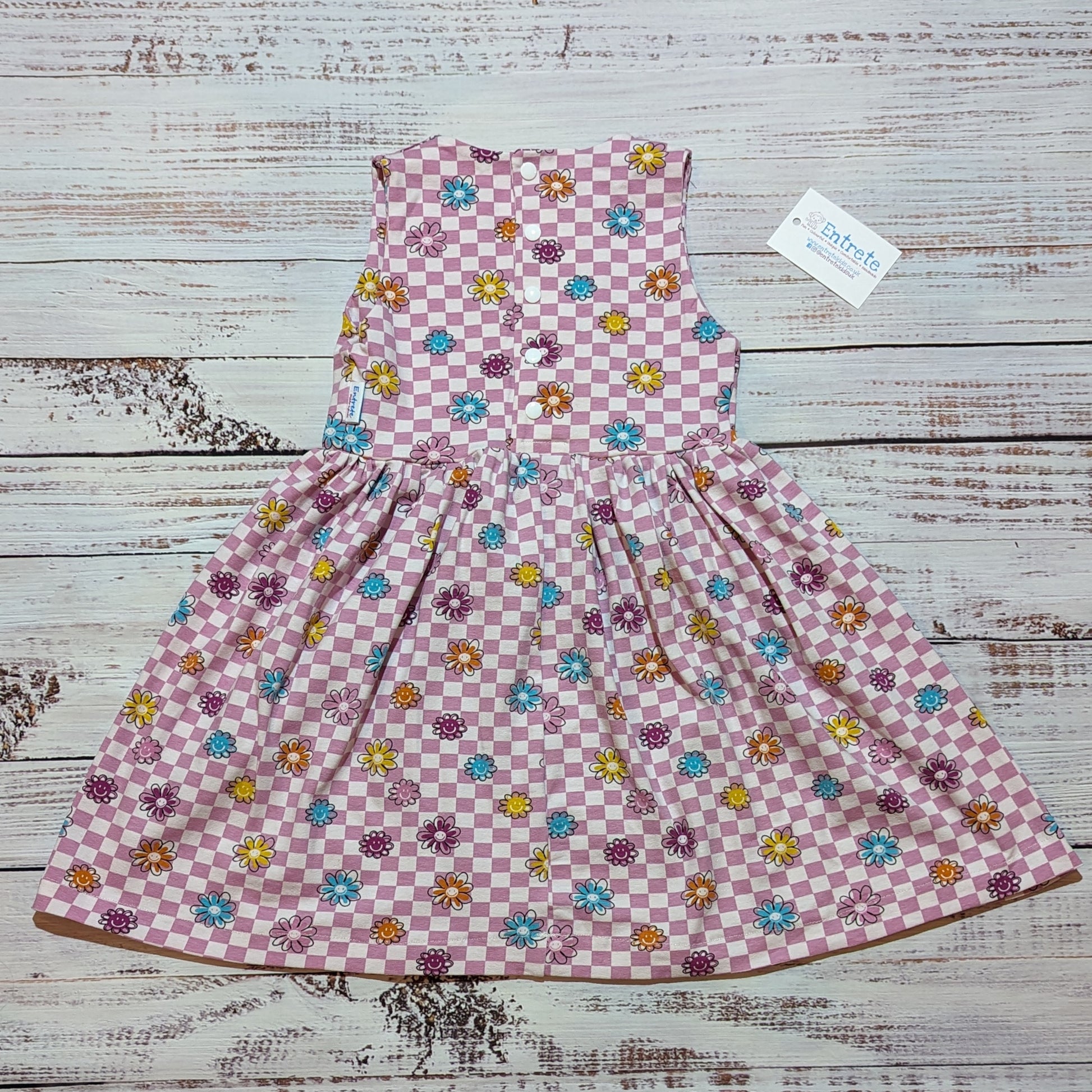 The adorable pink checked happy flowers dress. handmade in soft and comfy cotton jersey with a smiling flowers print. Shown from the rear.