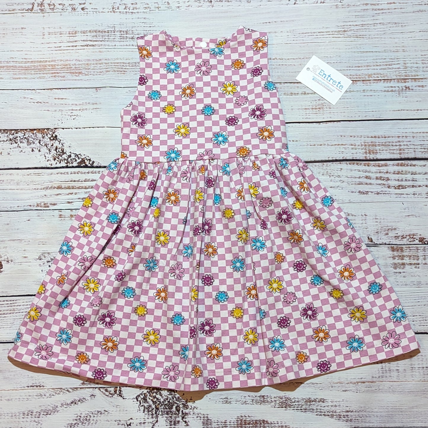 The adorable pink checked happy flowers dress. handmade in soft and comfy cotton jersey with a smiling flowers print. Shown as a sleeveless dress.