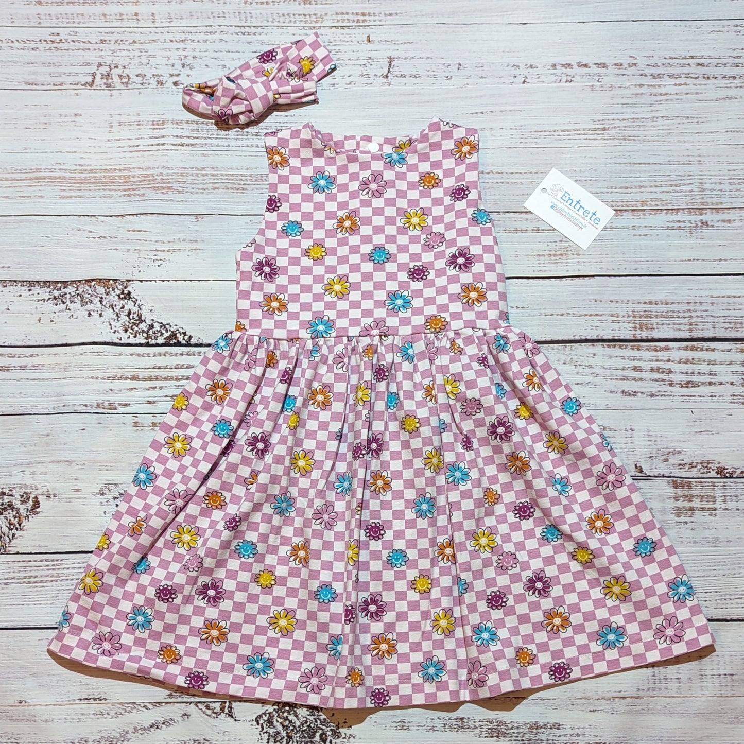 The adorable pink checked happy flowers dress. handmade in soft and comfy cotton jersey with a smiling flowers print. With a matching headband.