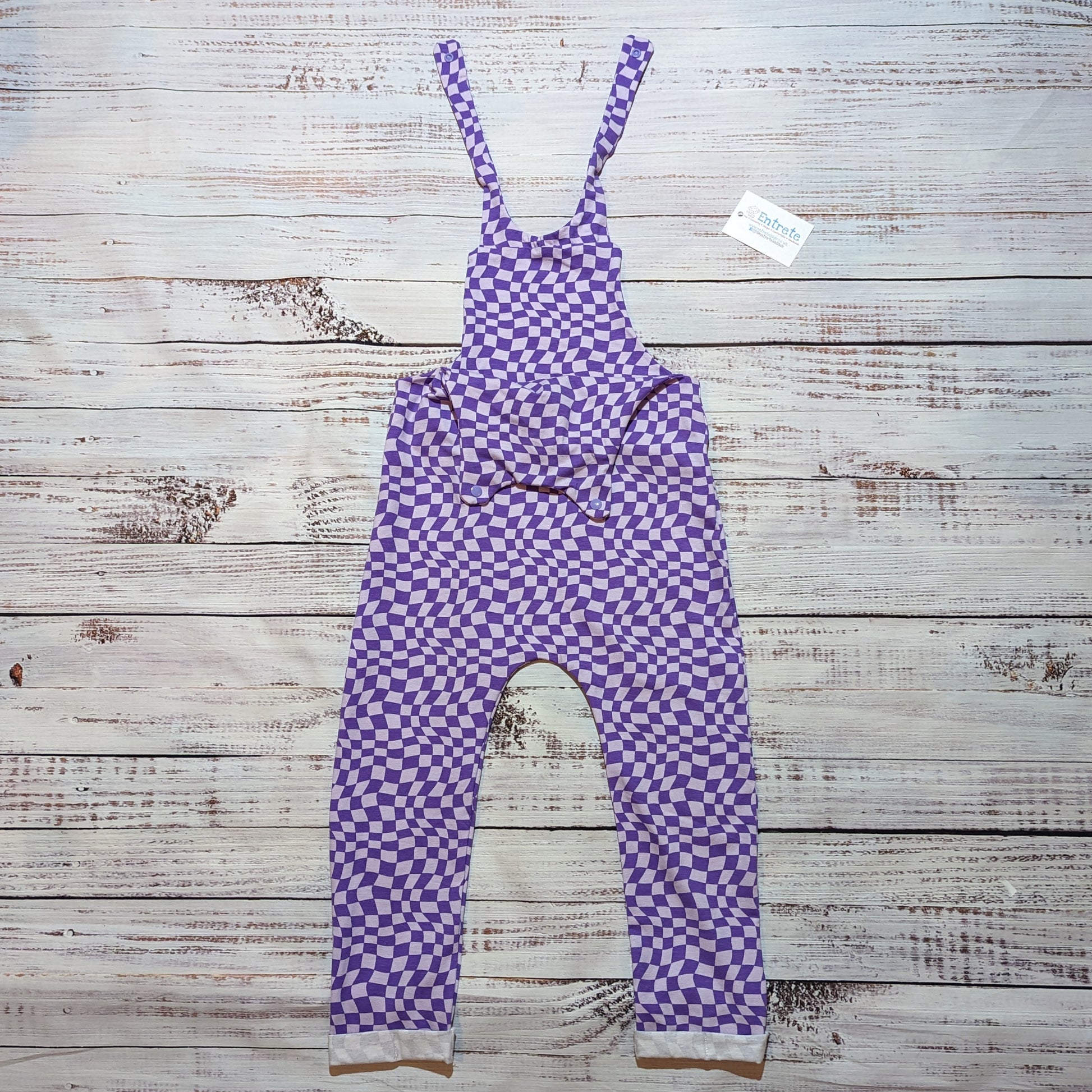 Kid's dungarees in a warped purple trippy checked print. Handmade in soft, stretchy and comfortable cotton jersey. Shown with the shoulder popper entry open.