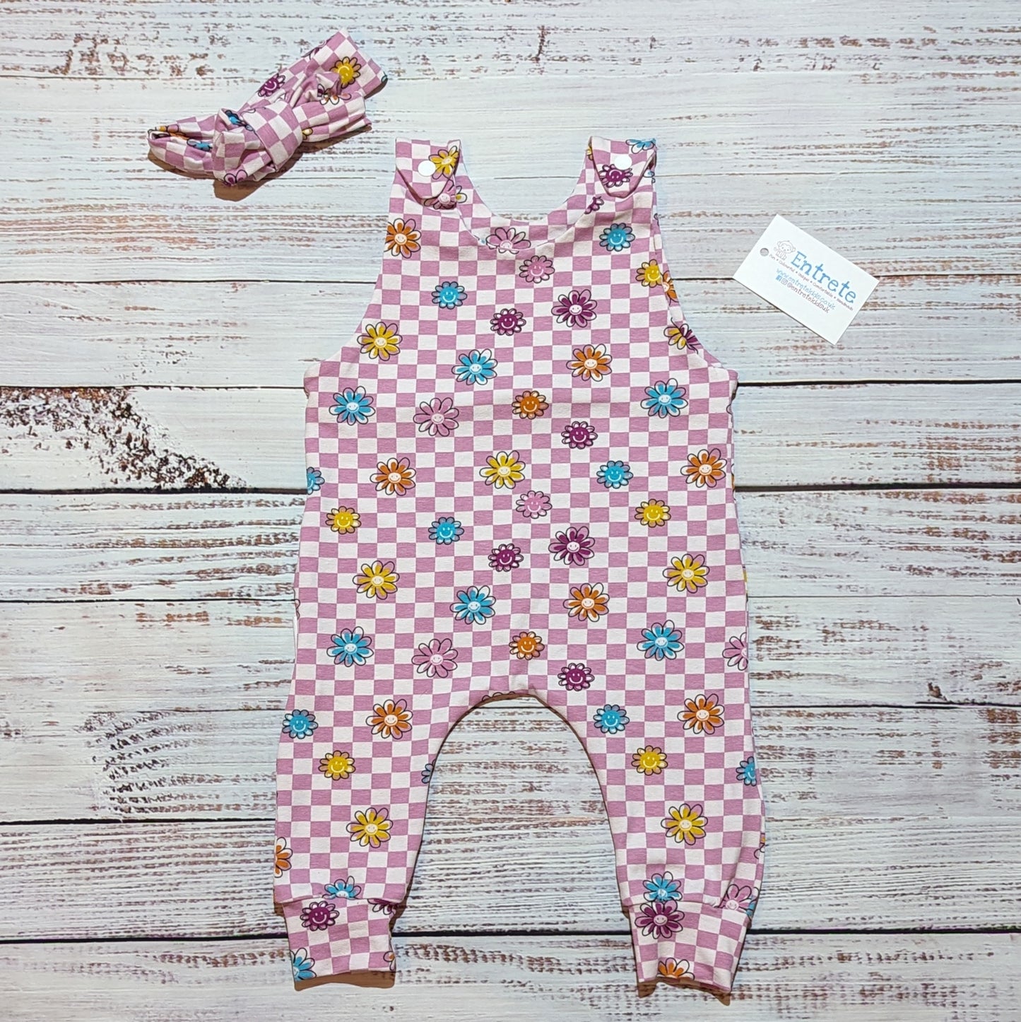 Pink checked happy flowers sleeveless romper. With shoulder popper entry and roll-able ankle cuffs. Handmade in soft and comfy cotton jersey. Shown with a matching headband.