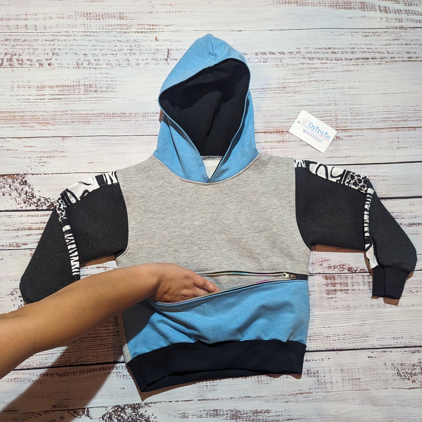 Sky blue, grey and animal hearts hoodie, with a zipped front pocket. Handmade using soft and comfortable cotton French terry. Demonstrating the zipped front pocket.