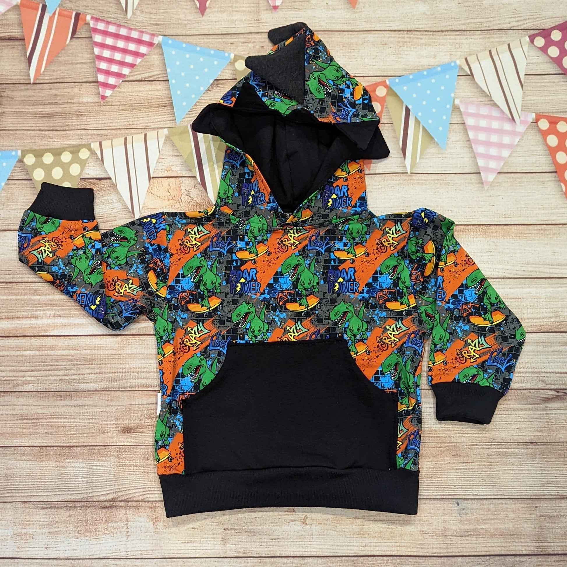 The Colourful and fun skateboarding dinosaur hoodie. Handmade using cool street dino cotton French terry, black cotton Jersey and graphite cotton ribbing. With spines and teeth on the hood and a contrasting front pocket.