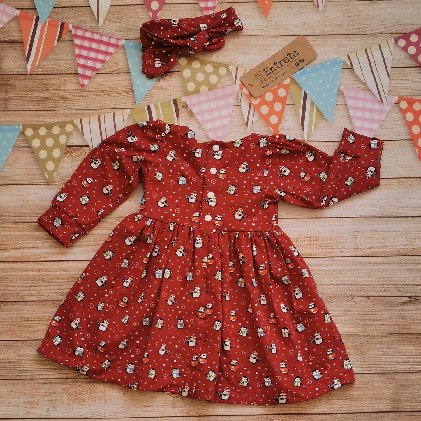 Rear view of Girls Christmas dress, handmade using the festive and fun red penguins cotton jersey. Shown with a matching headband (sold separately) This version has poppers to the waist as it will come for children over 9 months. Dresses under 9 months of size have buttons the length of the dress for easier changes.