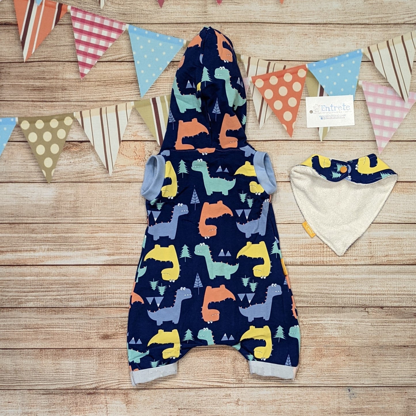 Fun and colourful dinosaurs hooded bummie romper. Handmade using blue dinosaurs and sky blue cotton jersey's with light blue cotton ribbing. Shown from the rear with a matching bamboo bib (sold separately)