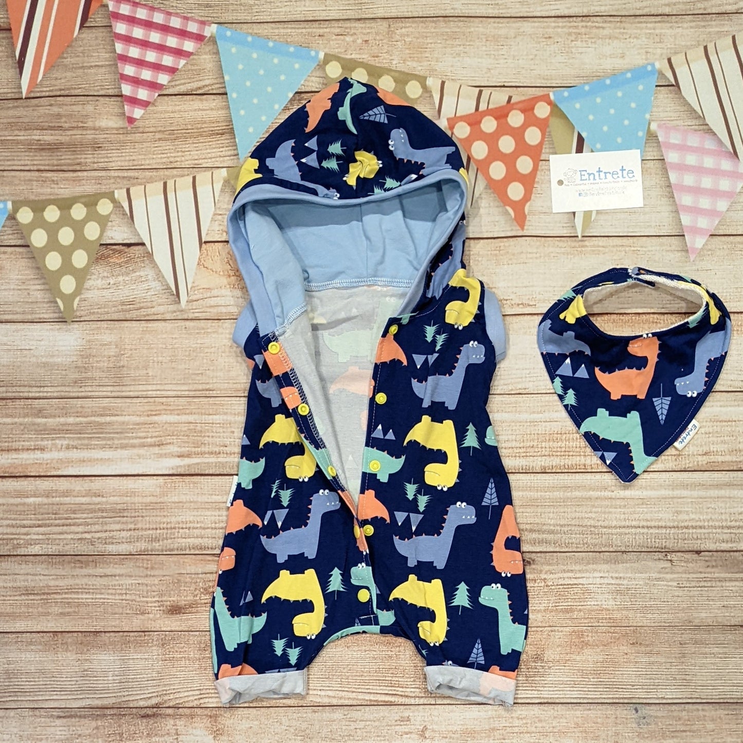 Fun and colourful dinosaurs hooded bummie romper. Handmade using blue dinosaurs and sky blue cotton jersey's with light blue cotton ribbing. Shown with the front popper entry open with a matching bamboo bib (sold separately)