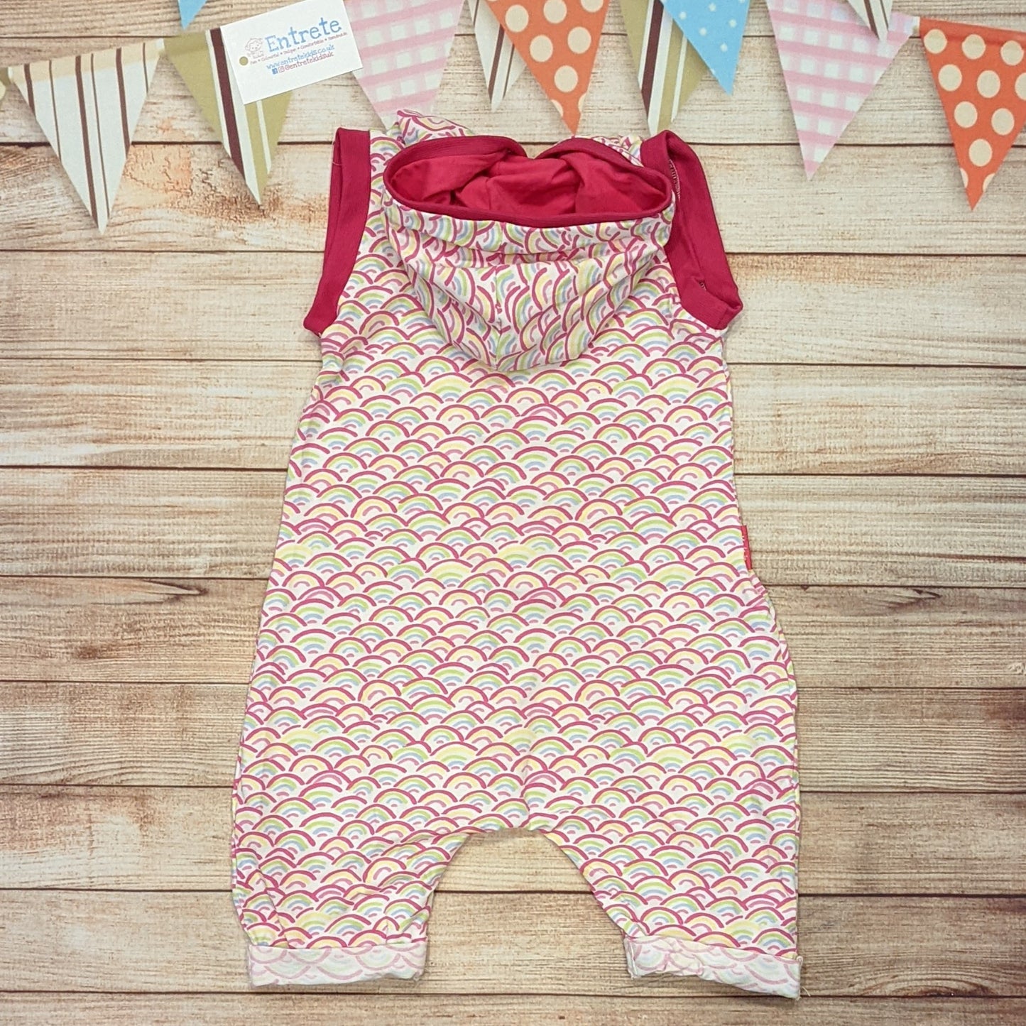 The adorable mini rainbows and fuchsia hooded bummie romper, perfect for the summer. Handmade using mini rainbows on white cotton jersey and fuchsia cotton jersey and cotton ribbing. Shown from the rear.