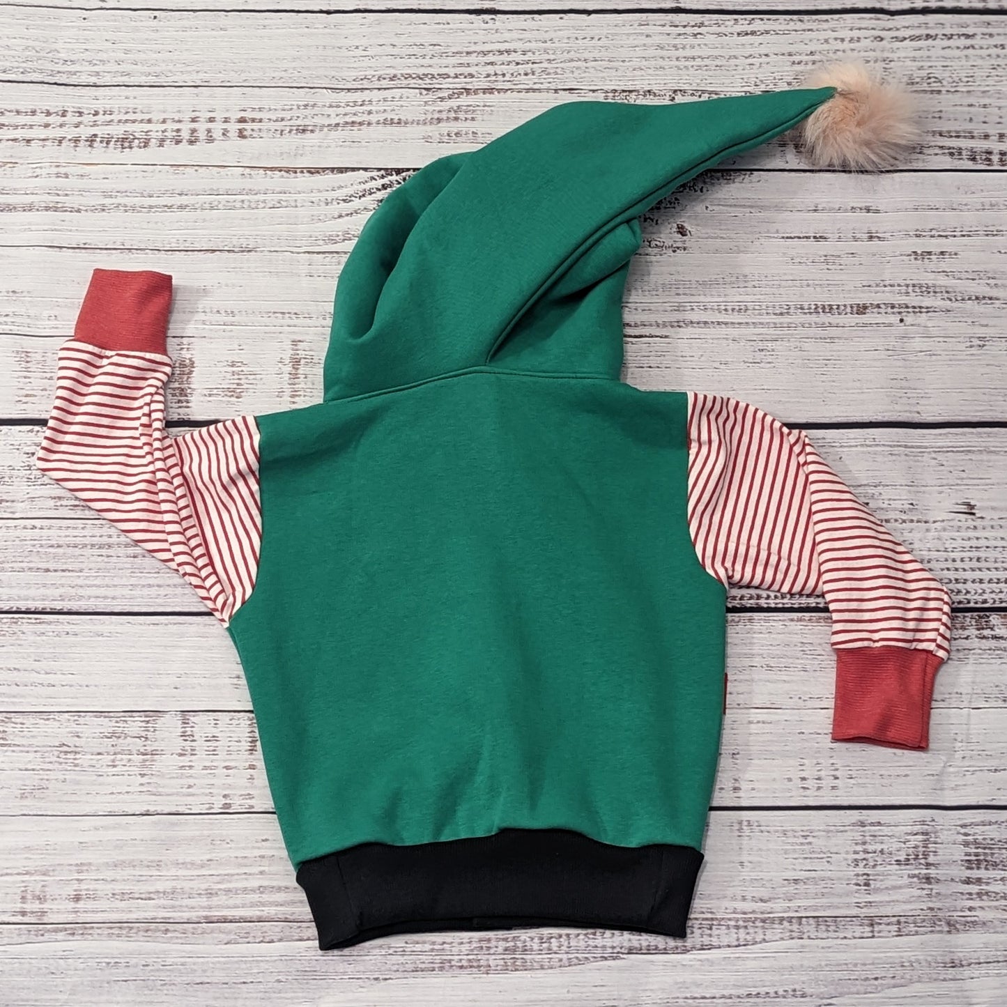 Rear view of the fantastically fun reversible elf hoodie. Handmade in green cotton sweatshirt fleece, with red striped cotton jersey arms, graphite ribbing waist and red ribbing cuffs . With adorable pom-pom hood.