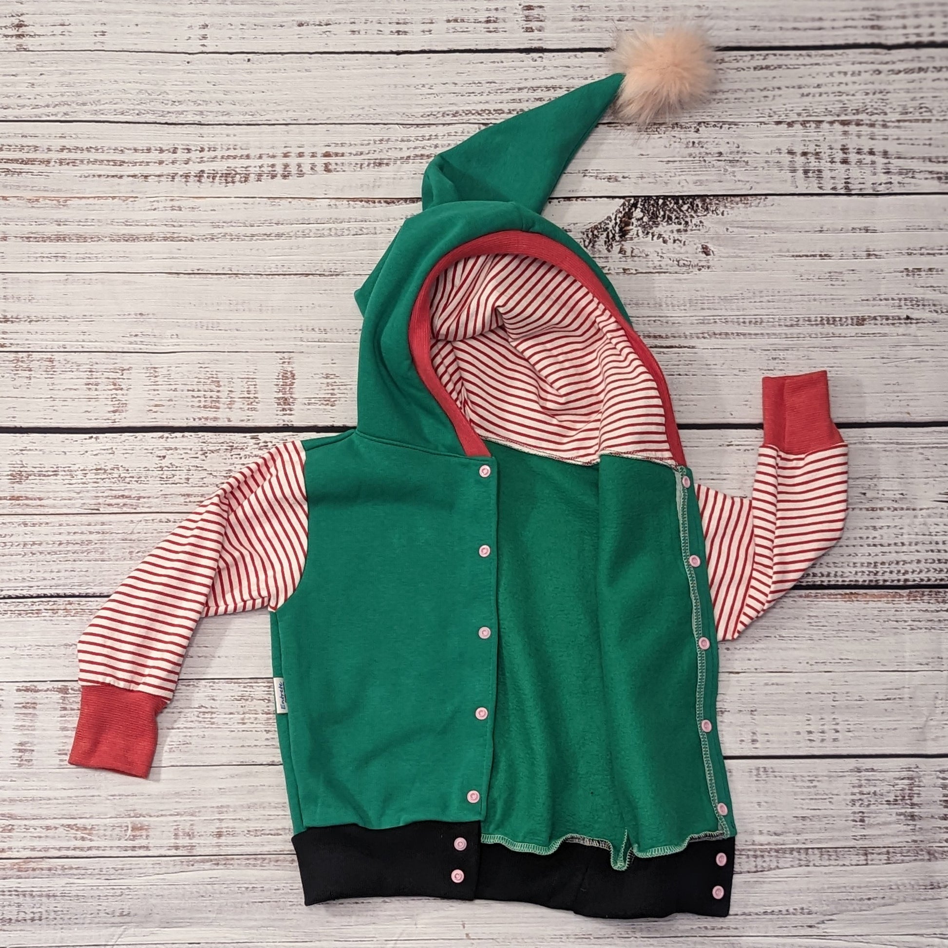 Fantastically fun reversible elf hoodie. Handmade in green cotton sweatshirt fleece, with red striped cotton jersey arms, graphite ribbing waist and red ribbing cuffs . With adorable pom-pom hood. Shown with popper entry open.