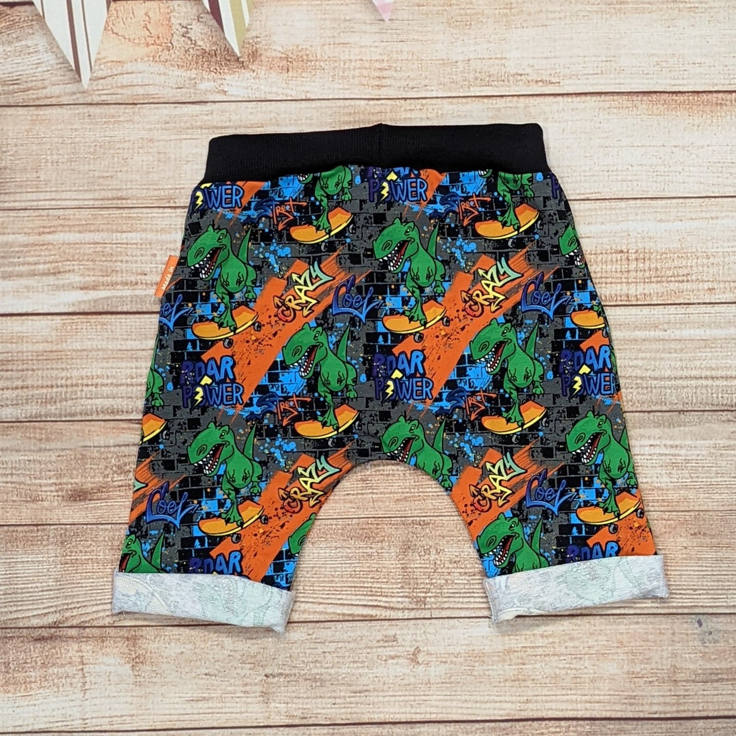 The insanely fun skateboarding dinosaurs harem shorts. Handmade using street dino cotton French terry and black cotton ribbing. Shown from the rear.