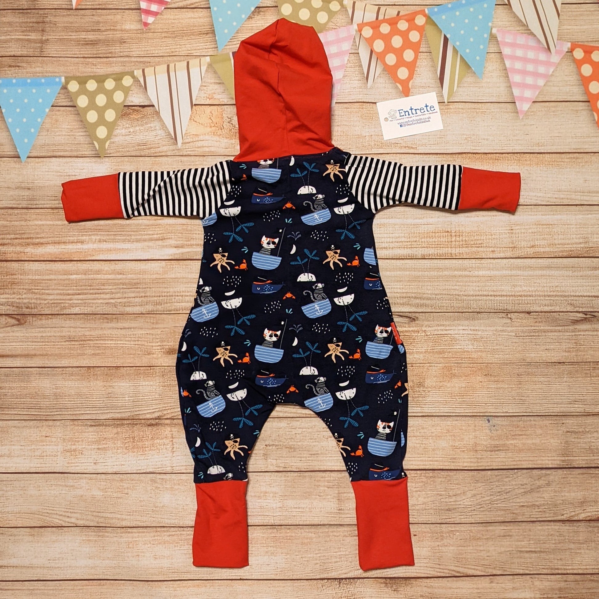 Fun and adventure await, with the awesome pirate cats hooded romper. Shown from the rear. Handmade using pirate cats, red and monochrome striped cotton jersey's.