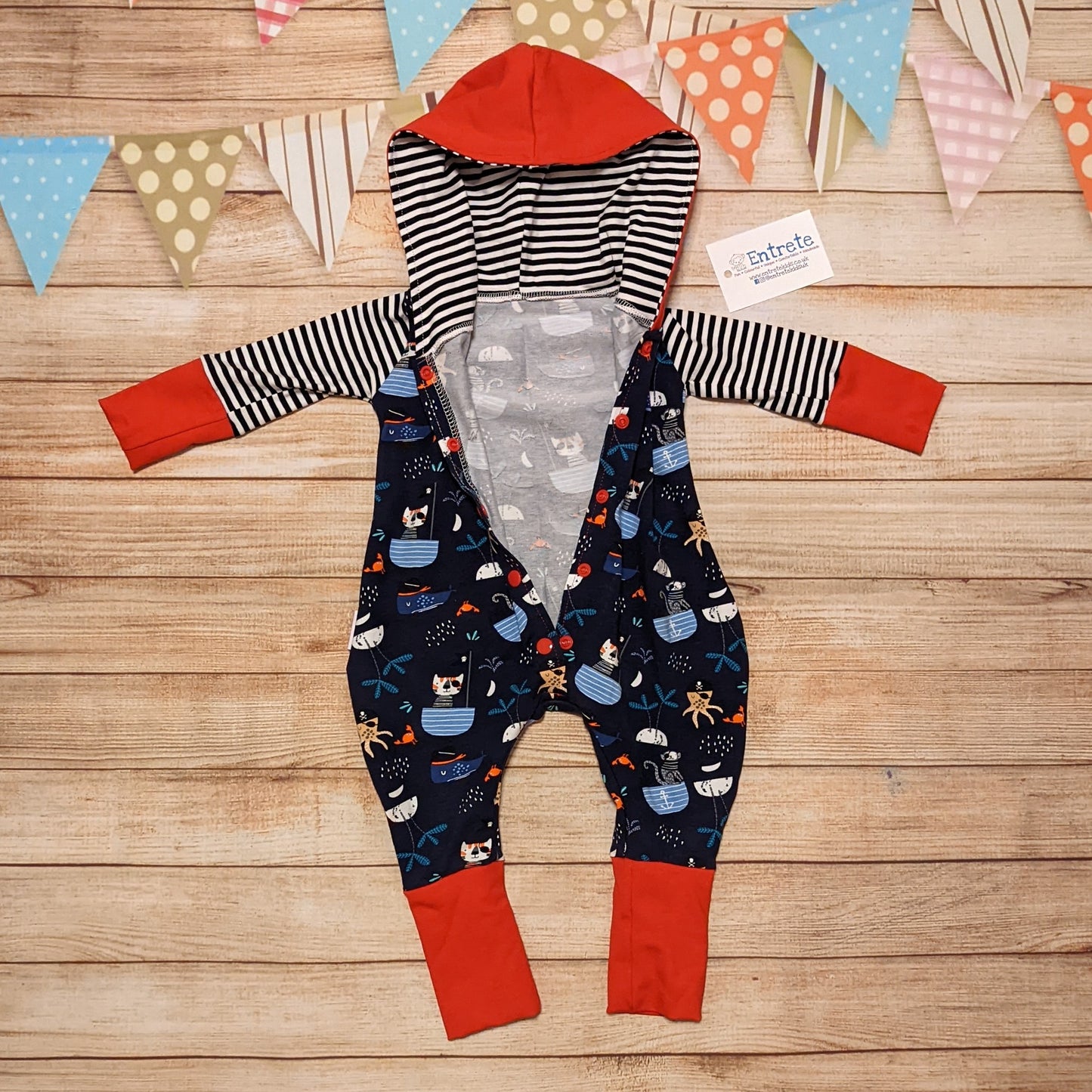 Fun and adventure await, with the awesome pirate cats hooded romper. Shown with the popper entry open. Handmade using pirate cats, red and monochrome striped cotton jersey's.