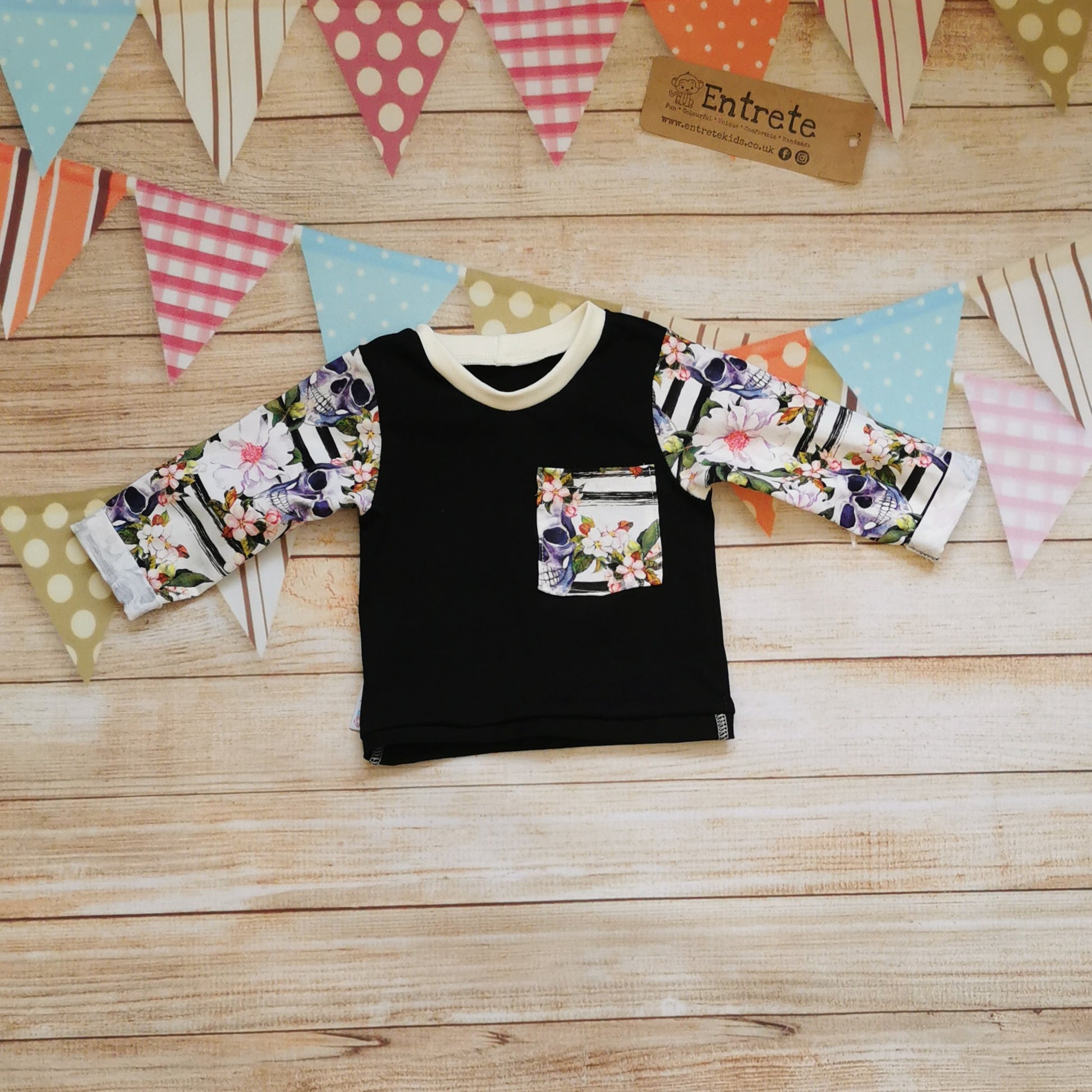 Front view of the stunning skulls and flowers long sleeved T. Handmade with gorgeously gothic skulls and flowers cotton jersey arms and front pocket on a contrasting black cotton jersey body. Featuring rolled cuffs and waist and ribbing on the neck. 