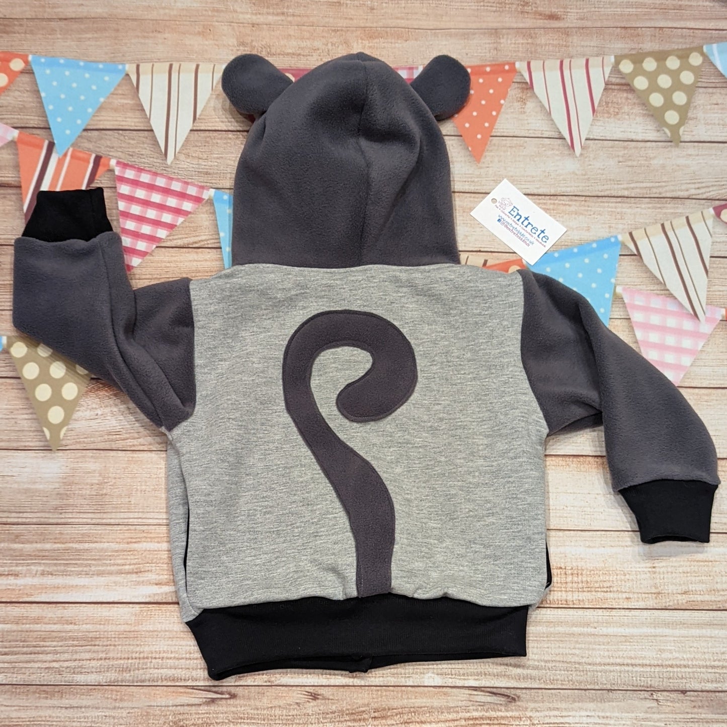 The reversible cat hoodie featuring fun tail and ear detailing. Handmade using grey polar fleece, light grey cotton french terry, black organic cotton jersey and graphite ribbing. The reverse is made using pink cheetah print cotton jersey. This cat hoodie is so unique and is great for imaginative play. Shown from the rear, with it's fun cats tail.