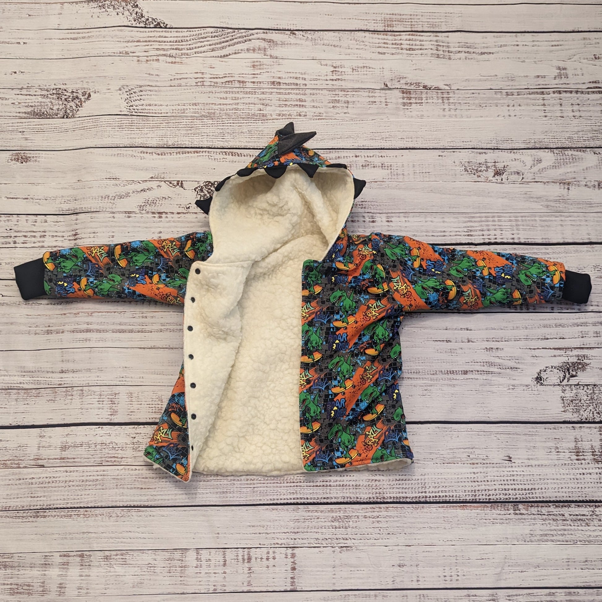 The ferociously cool street Dino reversible coat, shown with dinosaur teeth and spines for added fun. Handmade using street dino cotton French terry, black cotton ribbing and sherpa fur. With front popper entry open showing the warm sherpa fur inner.