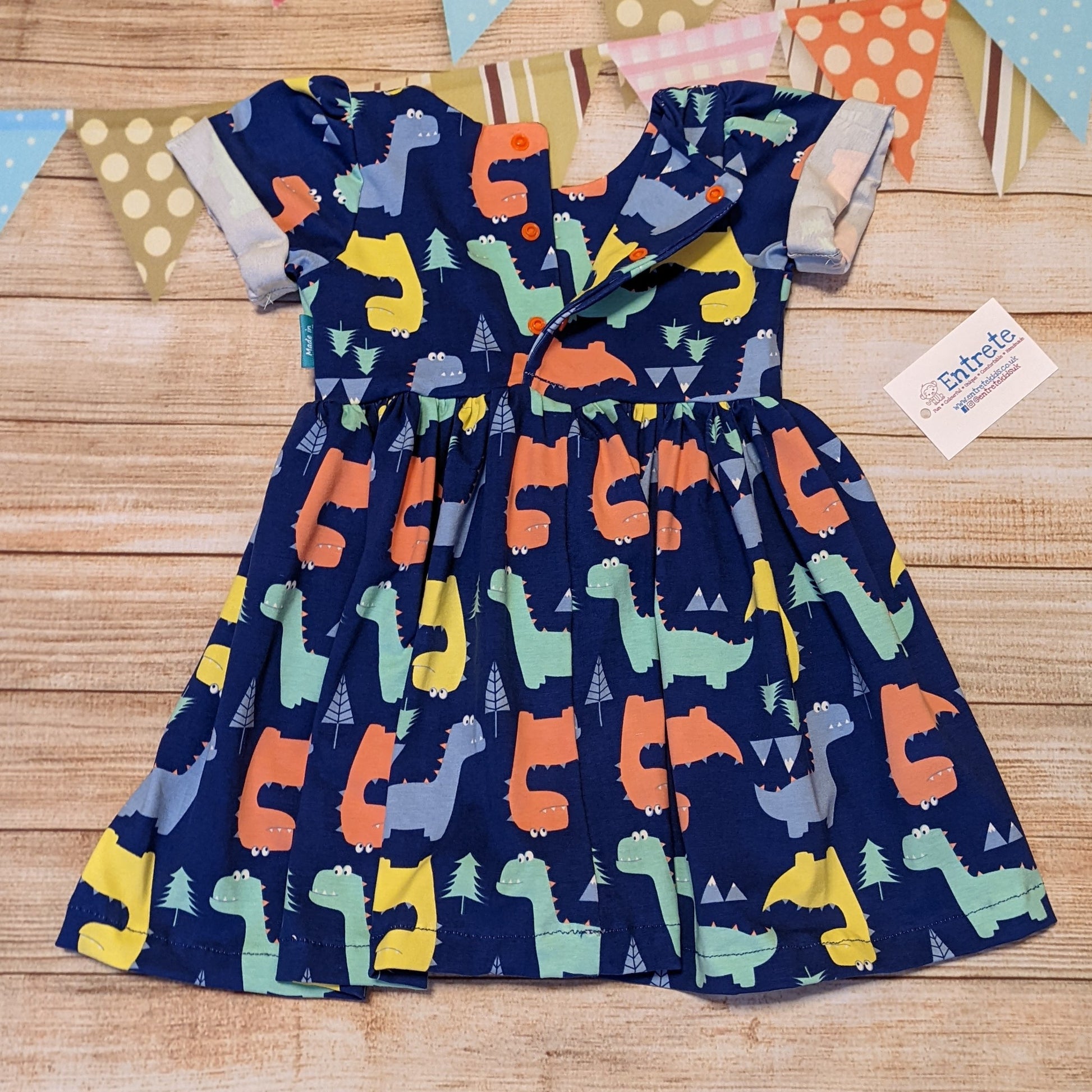 The short sleeved version of the colourful and fun blue dinosaur dress. Handmade using cotton jersey, featuring back poppers and rolled cuffs. Showing the rear popper entry.