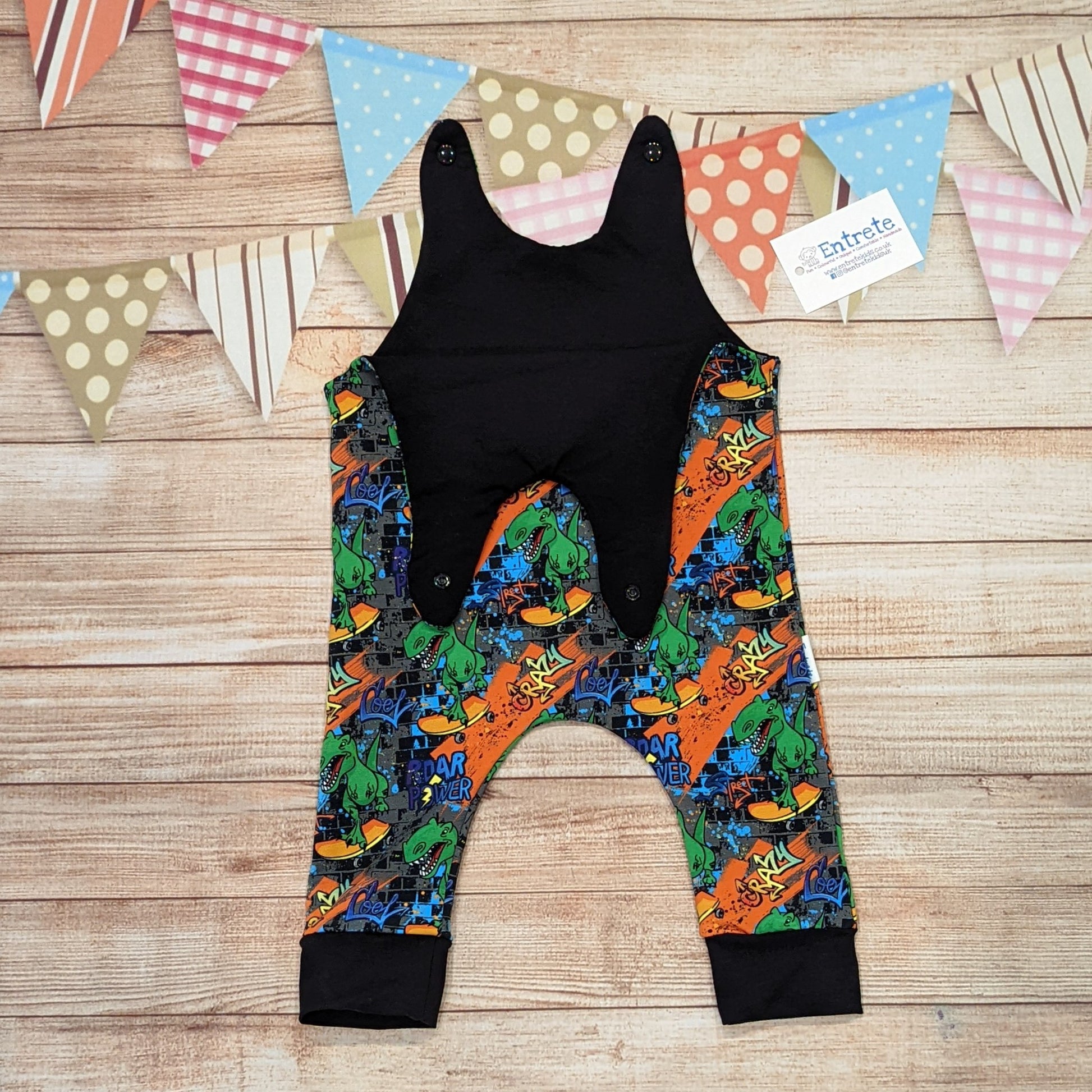 The insanely fun skateboarding dinosaurs romper. Handmade using street dino cotton French terry and black cotton jersey. Shown with the shoulder entry open.