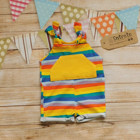 Front of Unisex Kids Tie Strap Dungaree Shorts, handmade using red rainbow striped cotton jersey and yellow organic cotton jersey. With rolled cuffs and tie shoulder straps that are infinitely adjustable, perfect for growing kids.