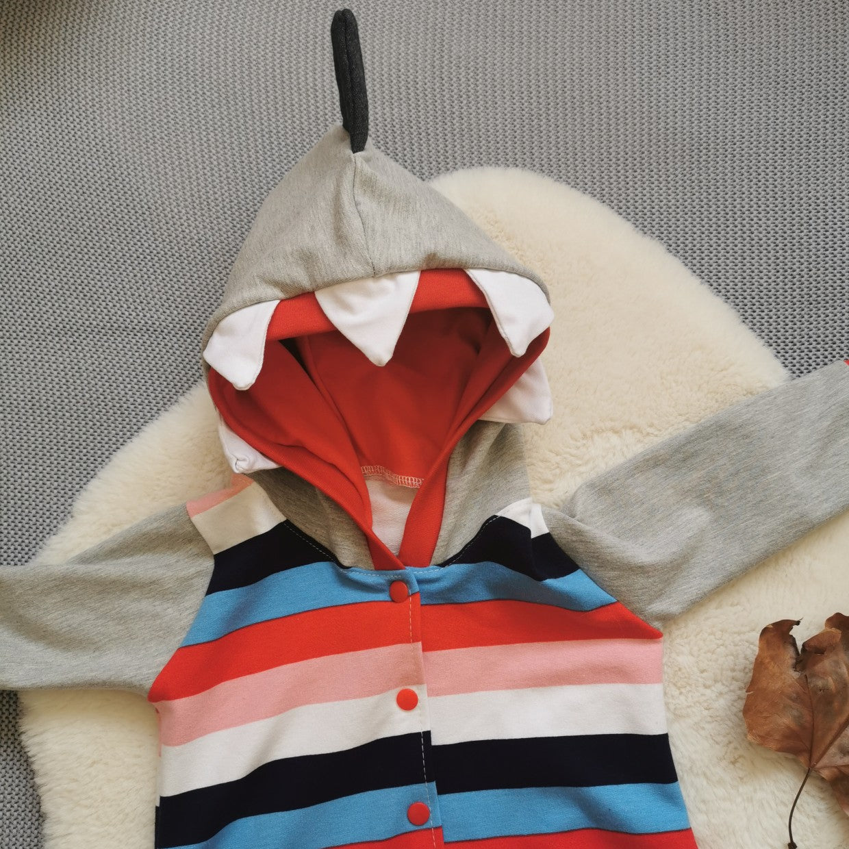 The warm, colourful and fun colour striped shark animal romper. Showing a close up of the shark hood with red mouth, white teeth and a grey shark fin! Handmade using colour striped cotton french terry, grey cotton sweat fabric and red cotton jersey.