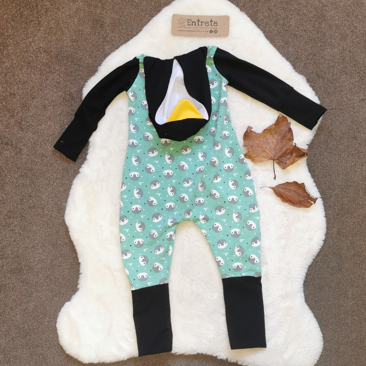 Rear view with folded hood of the ethical, fun and adorable penguin romper. Handmade using mint penguins, black and yellow organic cotton jerseys', with a natural bamboo hood lining. 