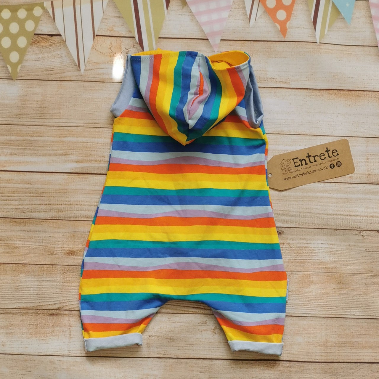 Rear of Unisex Kids Hooded Bummie Romper, handmade in gorgeous red rainbow striped cotton jersey, with yellow organic cotton jersey hood lining and light blue cotton ribbing.